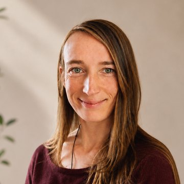 Portret van Lianne, de kunstenaar, glimlachend in een bordeauxrode trui.